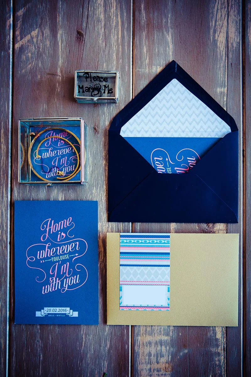 Papeterie de mariage bleue et or avec demande en mariage et cartes calligraphiées sur un fond en bois rustique.
