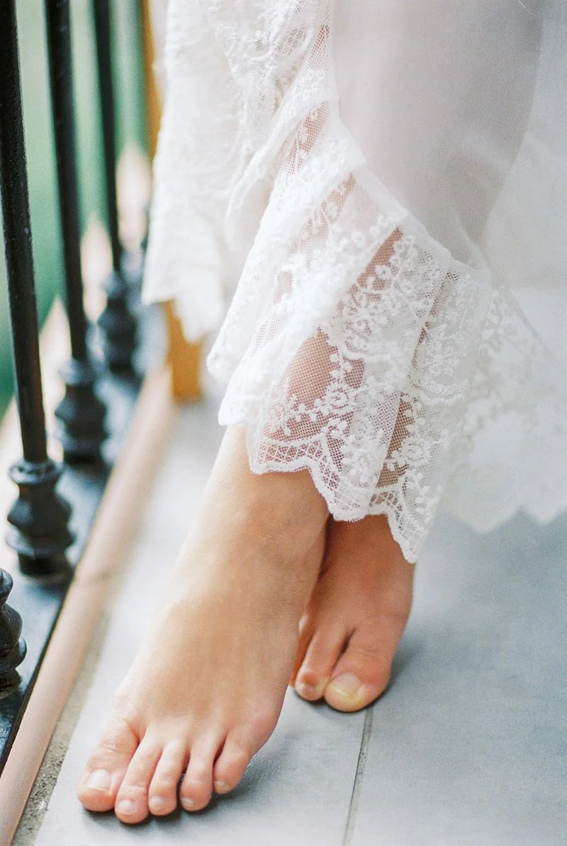 Pieds nus d'une mariée en robe de dentelle blanche, posés délicatement sur un sol gris.