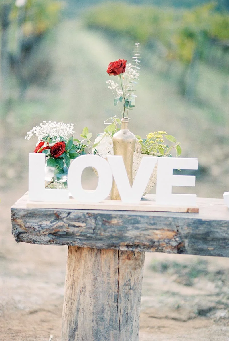 Lettres blanches formant le mot LOVE avec des roses rouges et du gypsophile sur un socle en bois rustique.