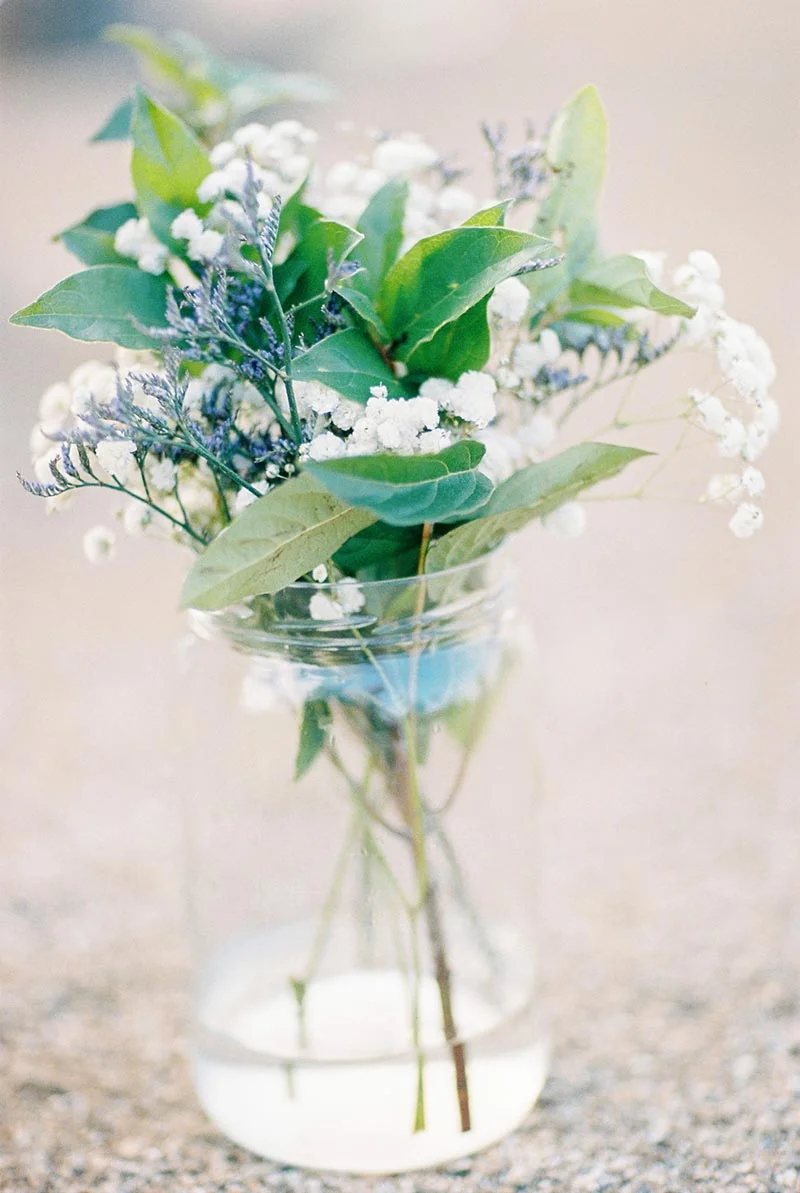 Bouquet champêtre de fleurs blanches et feuillage vert dans un vase en verre transparent, ambiance douce et lumineuse.
