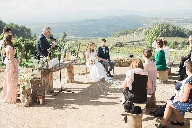 Cérémonie de mariage en plein air avec Julia et Maxime devant un officiant, entourés d'invités dans un paysage vallonné.