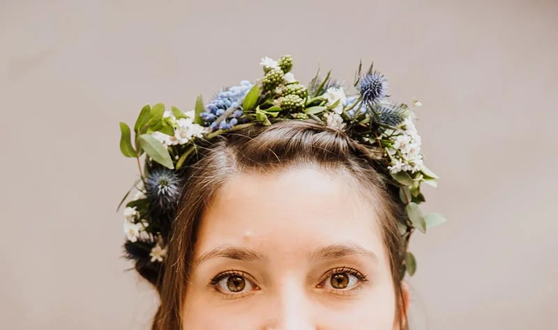 Portrait d'une mariée portant une couronne de fleurs sauvages bleues et blanches sur un fond neutre.