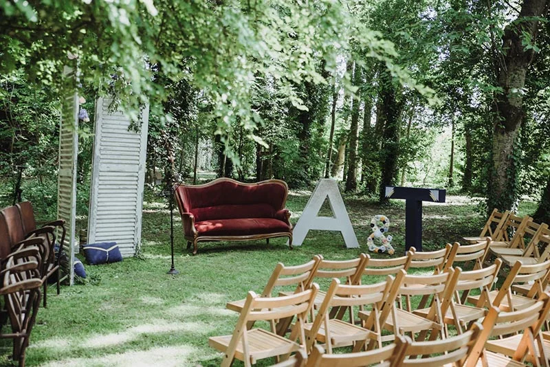 Décoration de mariage champêtre en forêt avec canapé rouge, lettres géantes A et T et chaises en bois.