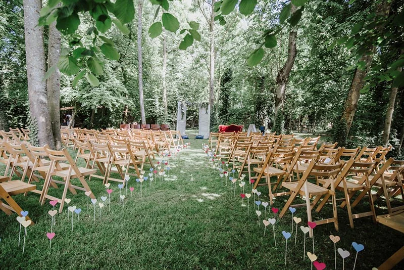 Chaises en bois alignées dans une forêt verdoyante pour une cérémonie de mariage romantique et naturelle.