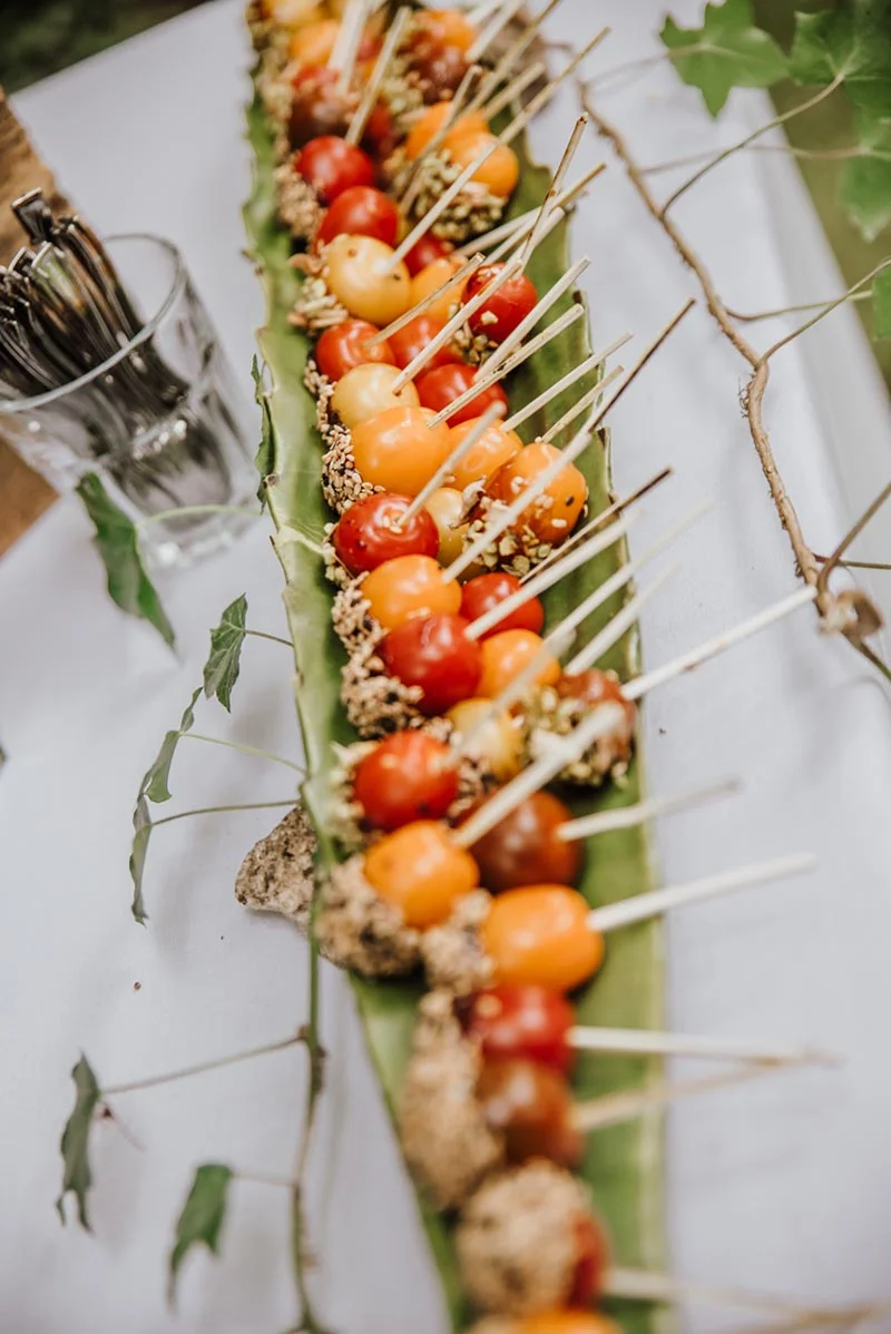 Brochettes de tomates cerises multicolores disposées sur une grande feuille verte pour un cocktail de mariage.