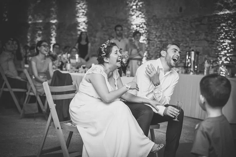 Jeunes mariés riant aux éclats lors de leur réception, photo en noir et blanc dans une ambiance festive et chaleureuse.