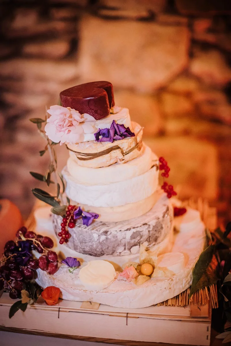 Pièce montée originale composée de meules de fromage, décorée de fleurs et de raisins sur un support en bois.