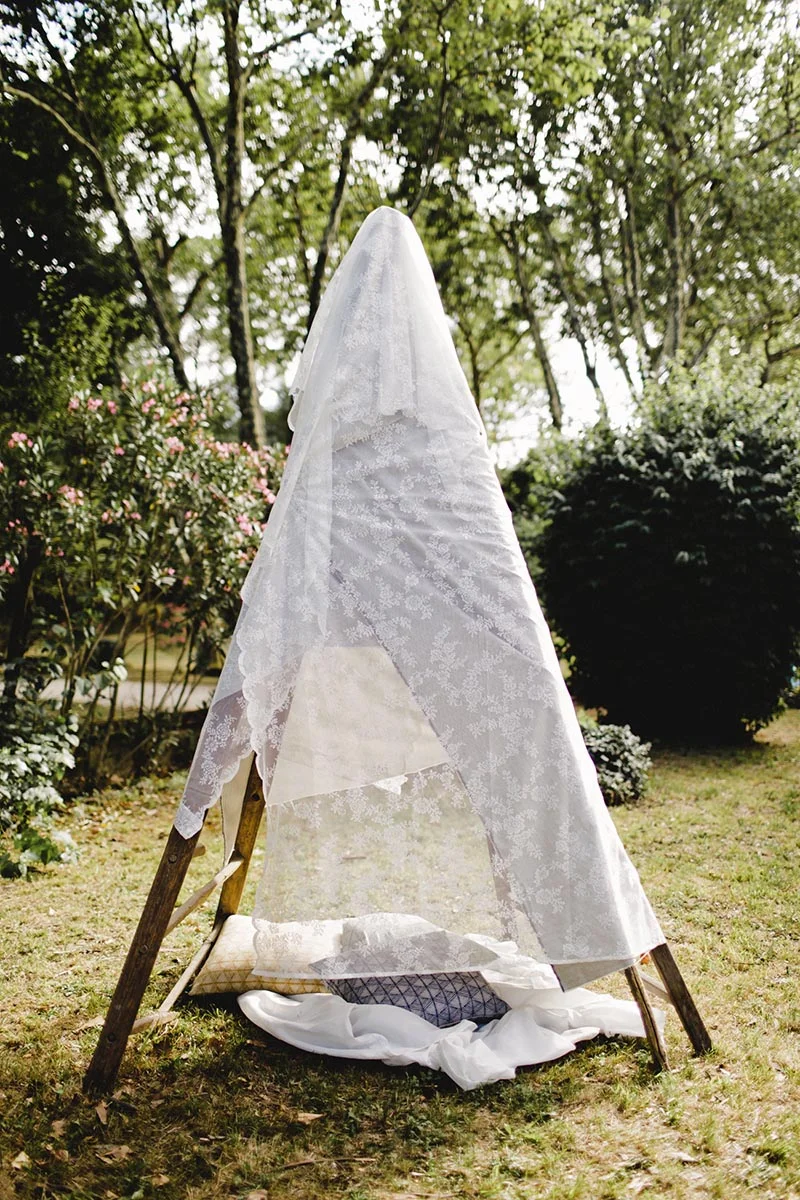 Tente tipi en dentelle blanche installée dans un jardin verdoyant pour une ambiance bohème et romantique.