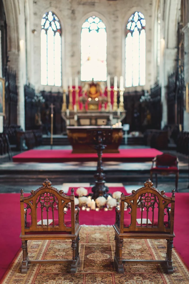 Intérieur d'une église solennelle avec deux chaises en bois sculpté et un tapis rouge devant l'autel lumineux.