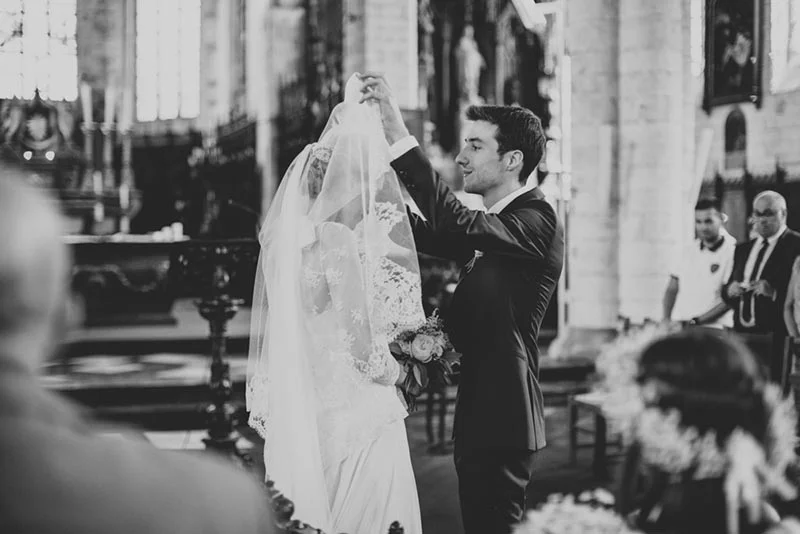 Photo noir et blanc d'un marié soulevant le voile de sa mariée dans une église lors de leur cérémonie de mariage.