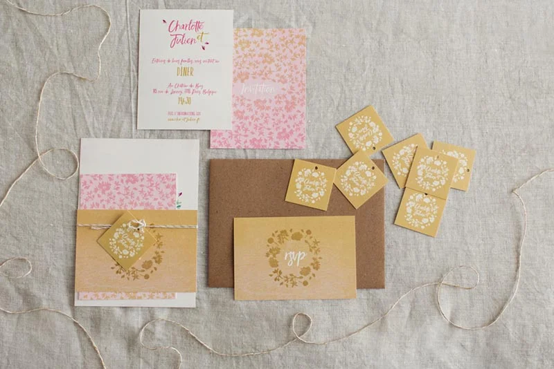 Papeterie de mariage beige et rose poudré avec invitations, enveloppes et étiquettes sur un fond en lin naturel.