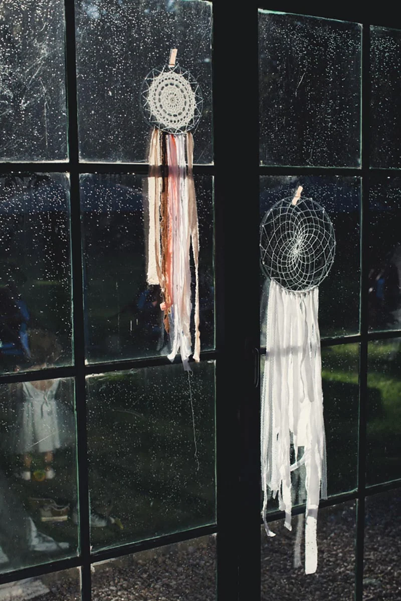 Deux attrape-rêves blancs et bohèmes suspendus à une fenêtre vitrée sous une pluie fine.