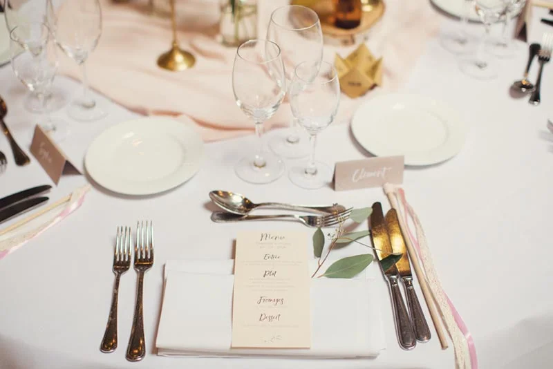 Dressage de table de mariage élégant et épuré dans les tons blanc et rose poudré avec menu et marque-places.