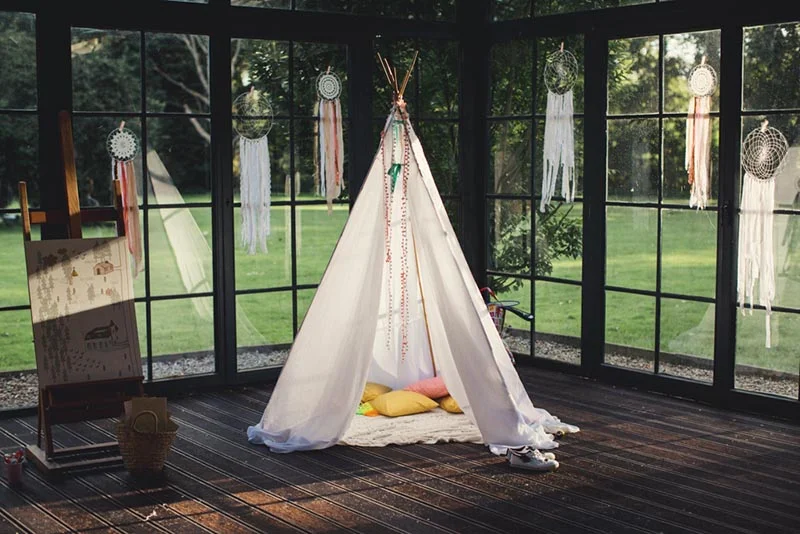 Tipi blanc décoré de capteurs de rêves sur une terrasse en bois, ambiance bohème et lumineuse pour un mariage.