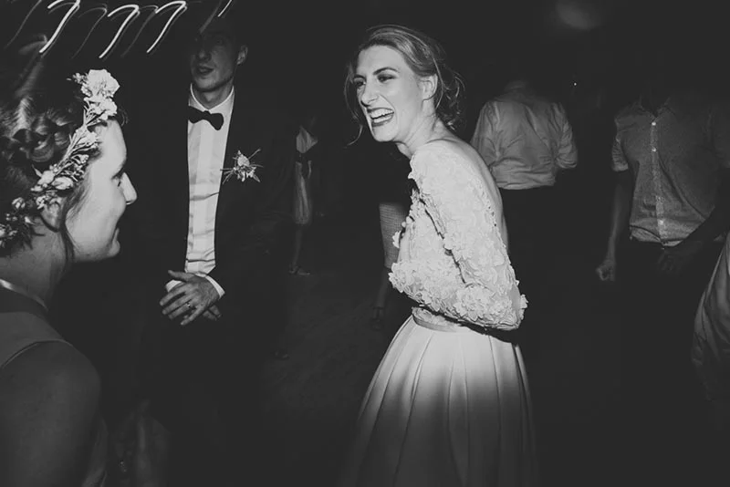 Mariée rayonnante en robe blanche riant avec ses invités lors d'une soirée de mariage, cliché en noir et blanc.