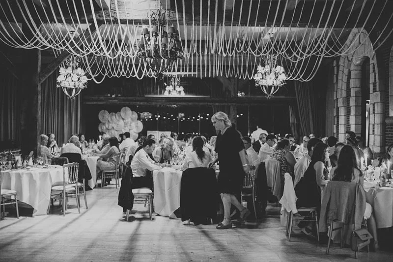 Réception de mariage en noir et blanc avec tables dressées sous des guirlandes de tissu et des lustres élégants.