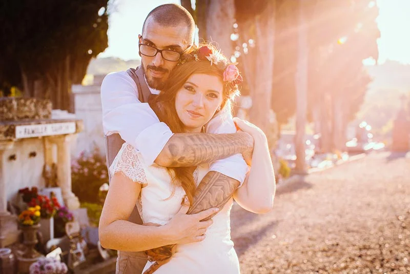Couple marié s'enlaçant tendrement dans un cimetière baigné d'une lumière dorée et chaleureuse.
