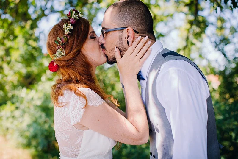Jeunes mariés s'embrassant tendrement en extérieur, la mariée portant une couronne de fleurs et une robe en dentelle.