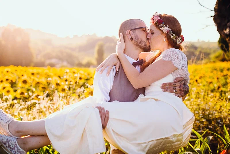 Jeune couple marié s'embrassant tendrement dans un champ de tournesols sous une lumière dorée.