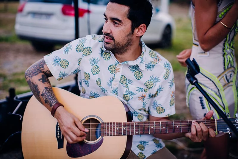 Un musicien en chemise à motifs ananas joue de la guitare acoustique lors du mariage de Virginie et Stéphane.