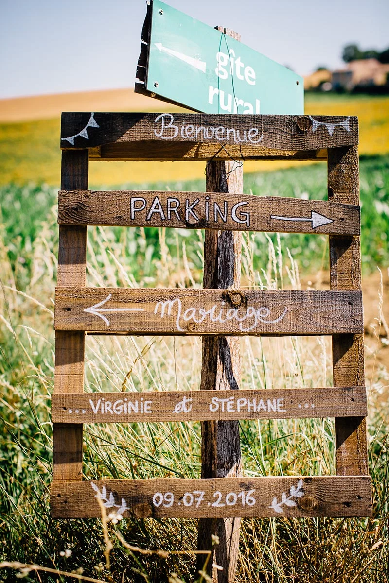 Panneau directionnel en bois rustique pour le mariage de Virginie et Stéphane dans un champ ensoleillé.