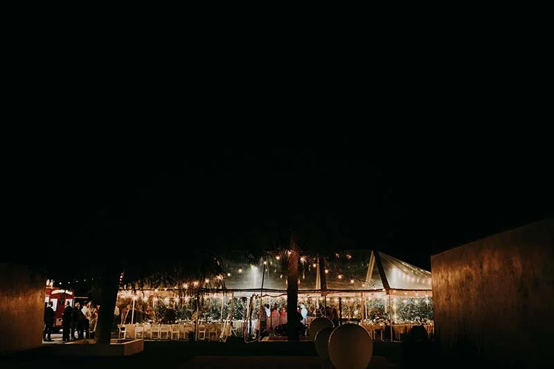 Réception de mariage nocturne sous un chapiteau transparent illuminé de guirlandes, ambiance chaleureuse et romantique.