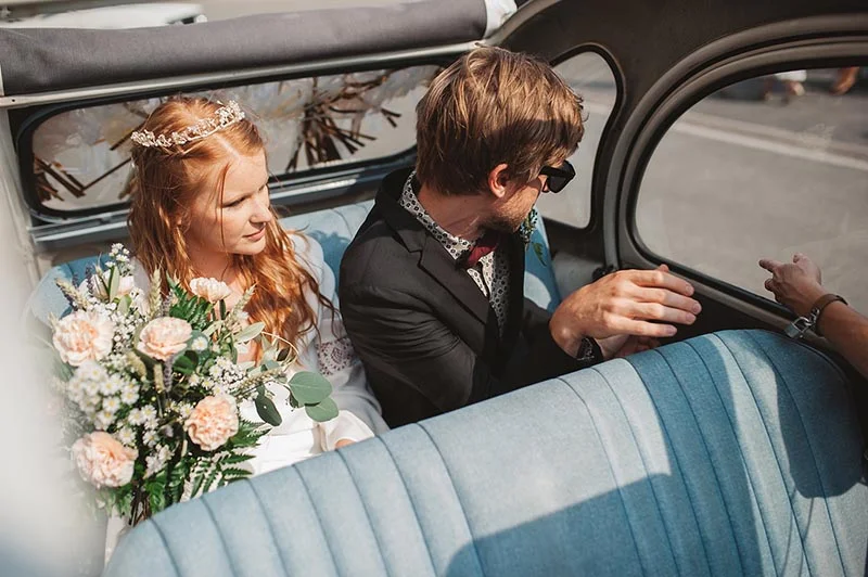 Jeunes mariés dans une voiture vintage bleue, ambiance bohème et romantique.