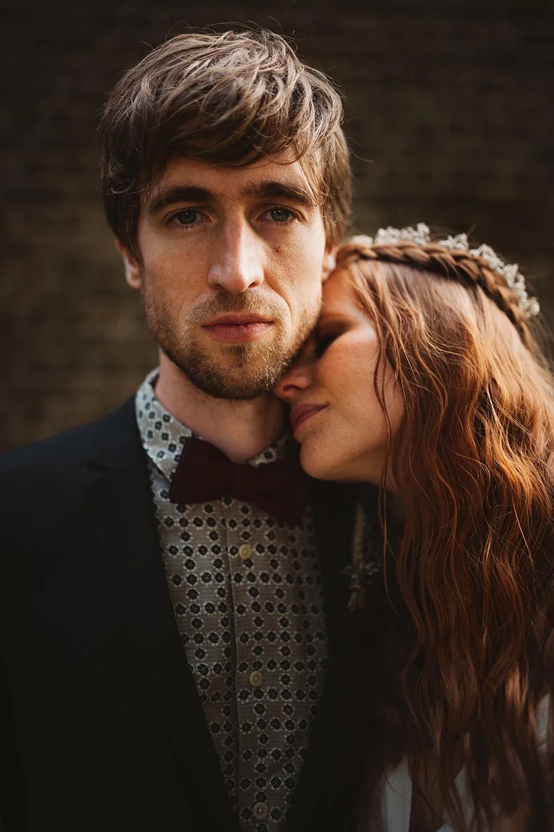 Un couple de mariés s'enlace tendrement, lui en costume et nœud papillon, elle avec une couronne de fleurs dans ses cheveux.