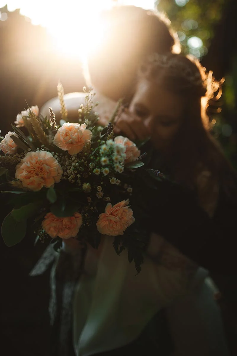 Jeune couple s'enlaçant tendrement avec un bouquet de fleurs pêche dans une ambiance lumineuse et romantique.