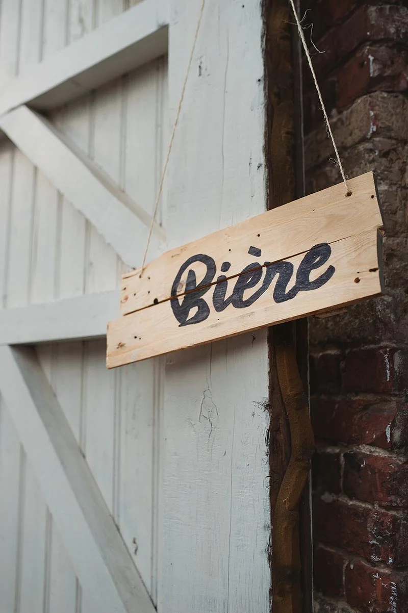 Panneau en bois rustique indiquant Bière, suspendu à une porte blanche devant un mur de briques rouges.
