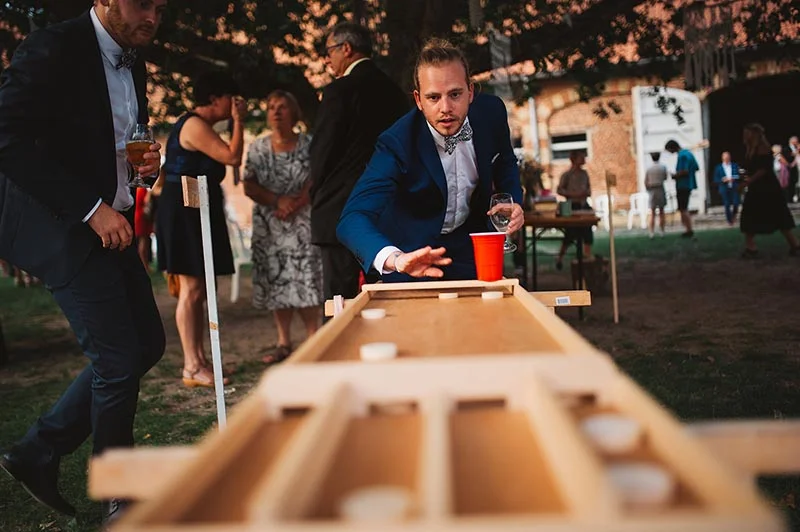Un homme en costume bleu joue au beer pong lors d'un mariage convivial en extérieur.