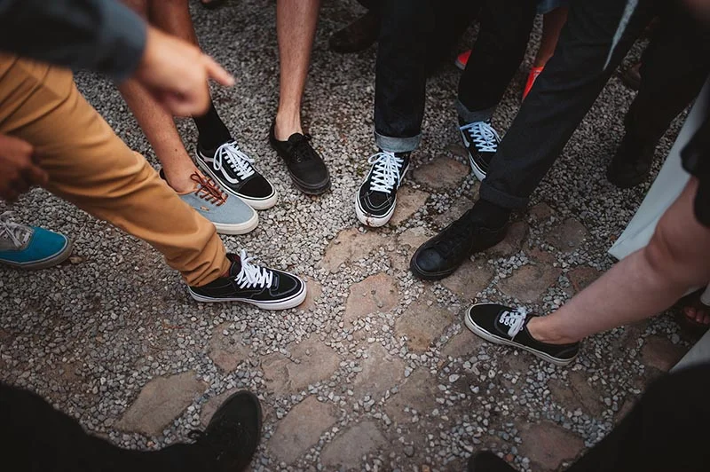 Vue en plongée de plusieurs personnes en baskets et pantalons décontractés debout sur un sol en gravier et pierres.
