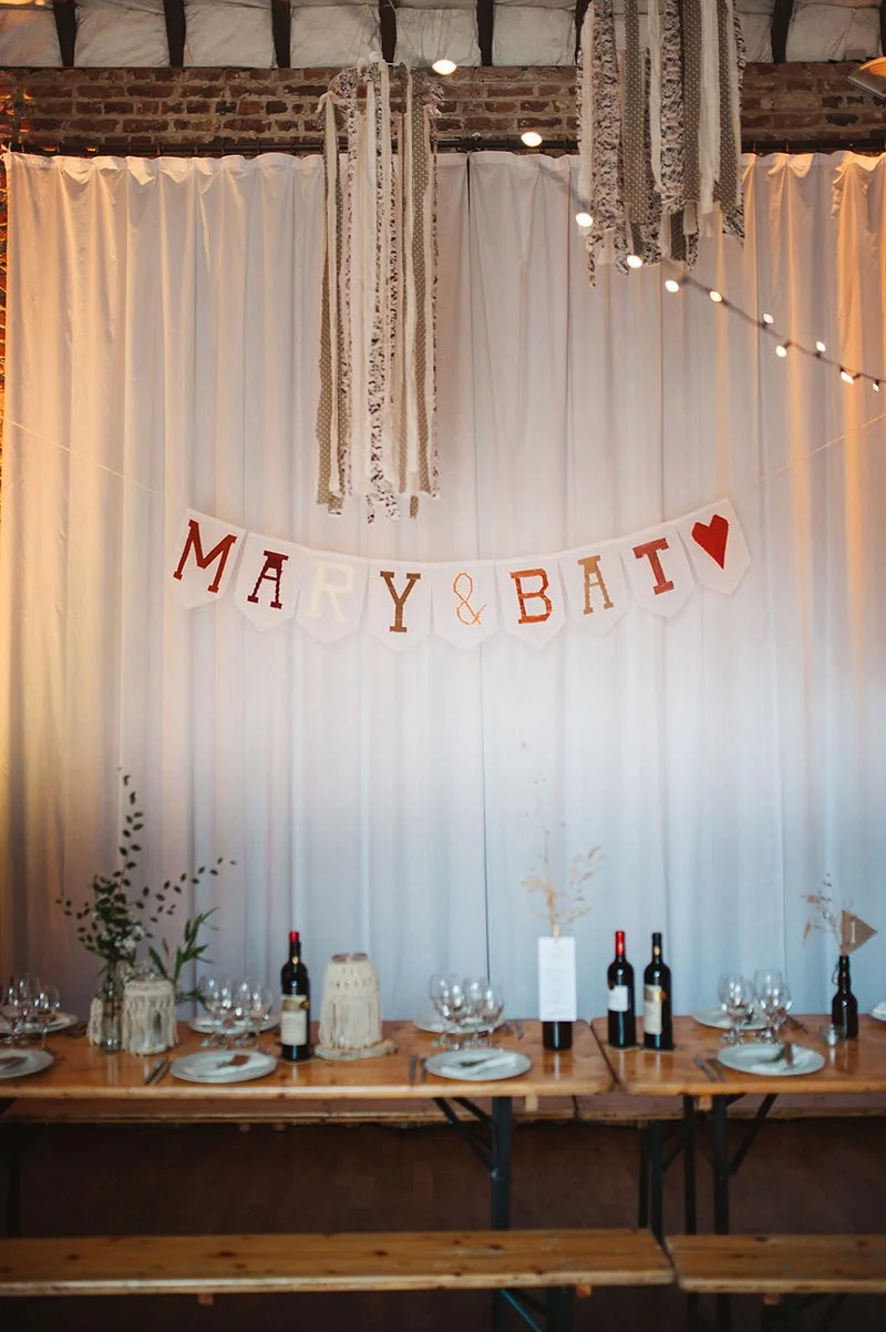 Décoration de table rustique avec guirlande "MARY & BATI" devant un rideau blanc et des touches bohèmes.