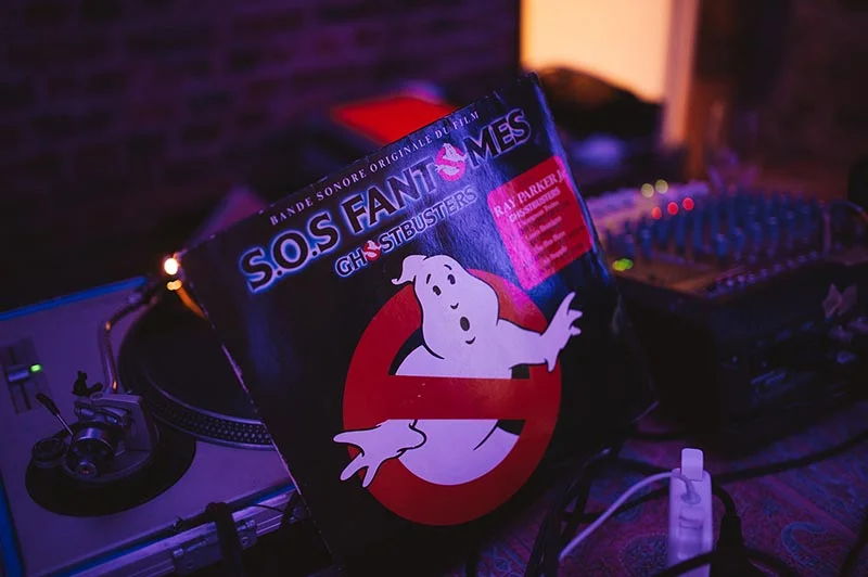 Vinyle de la bande originale de Ghostbusters posé sur un platine DJ dans une ambiance tamisée et colorée.