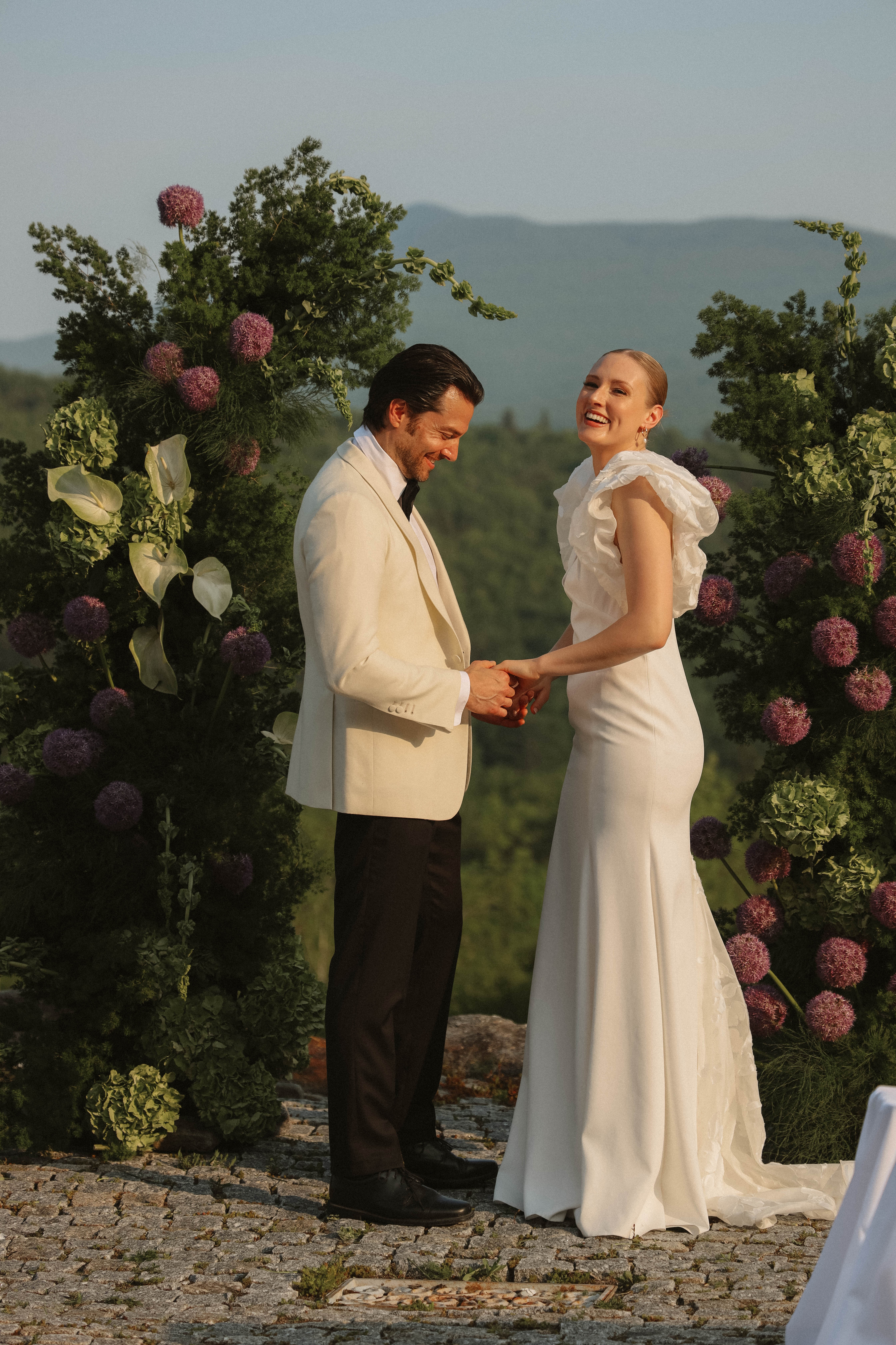 Couple souriant lors d'une cérémonie minimaliste en plein air, entouré d'arches florales sauvages et verdoyantes.