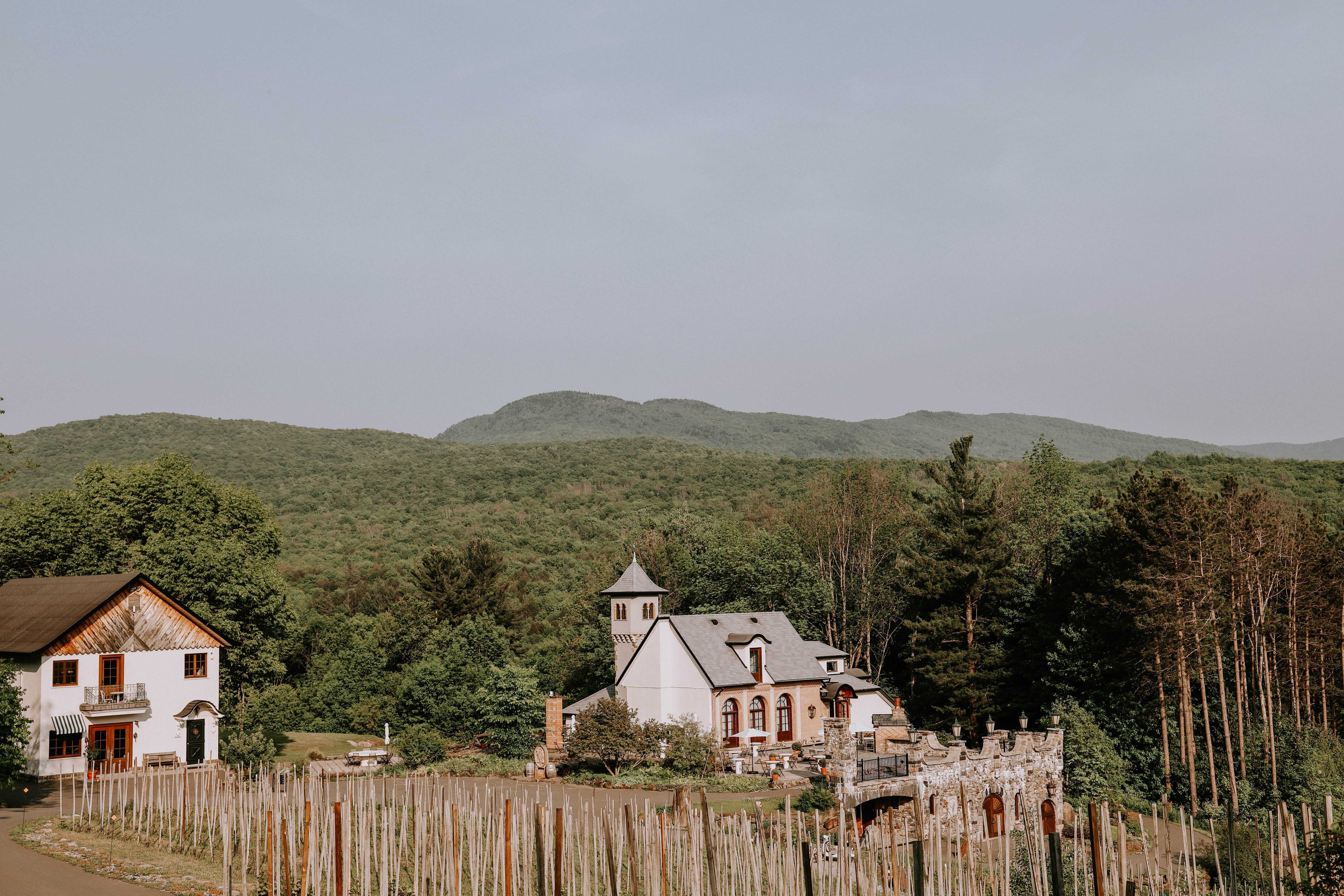 Maison de campagne blanche et jardin rustique au pied de collines verdoyantes sous un ciel doux et lumineux.