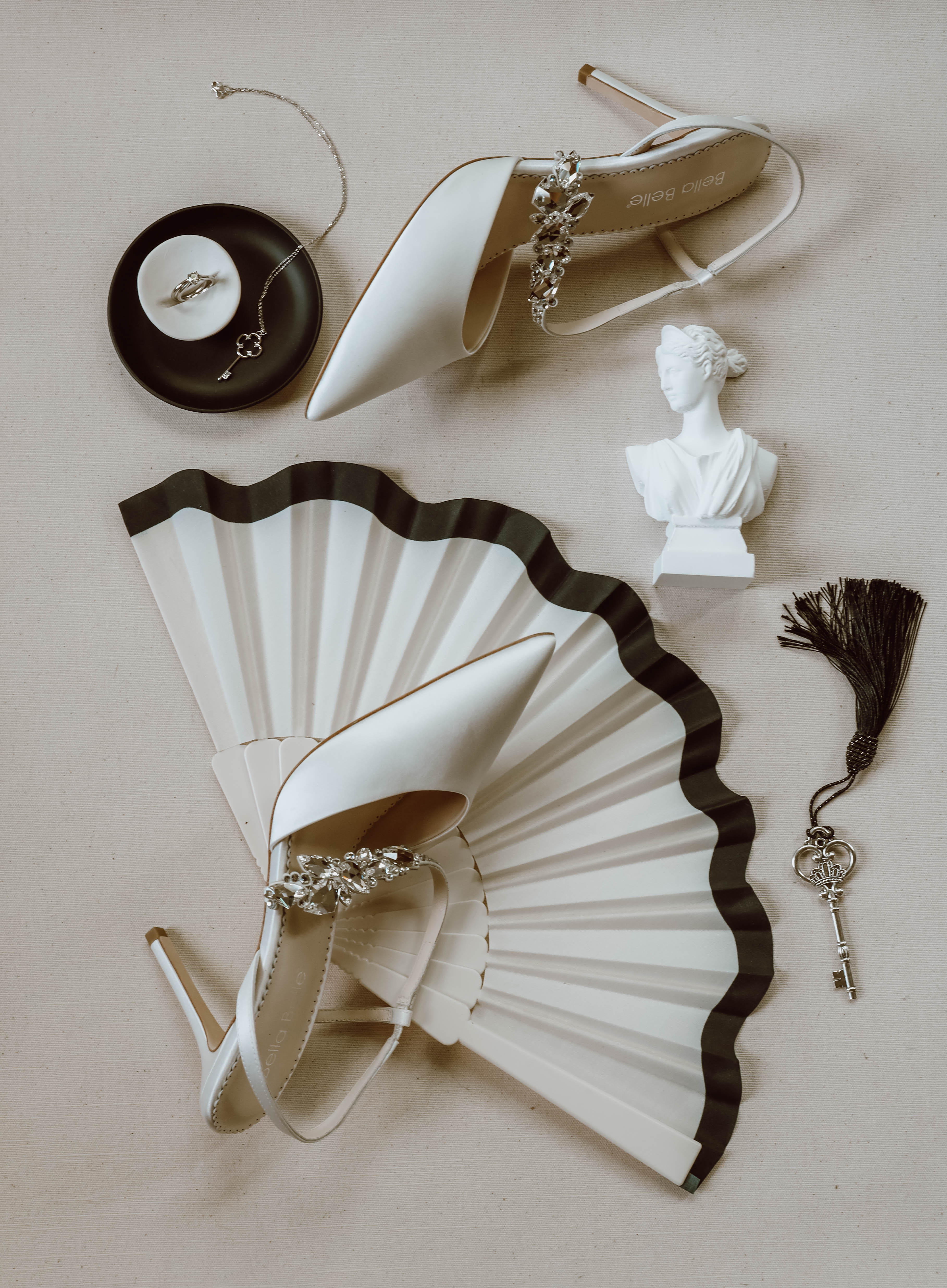 Composition minimaliste d'escarpins blancs, d'un éventail et d'accessoires élégants sur un fond neutre.