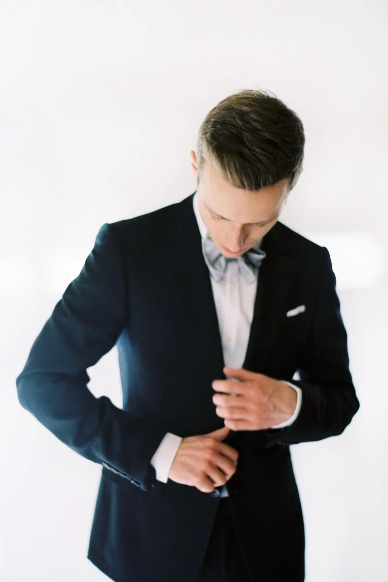 Un jeune homme en costume classique ajustant son veston, prêt pour un événement majeur.