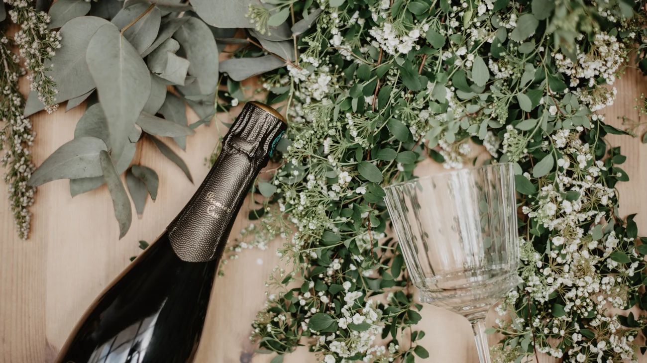 Boutellle et verre de champagne vus de haut sur un lit de feuillage