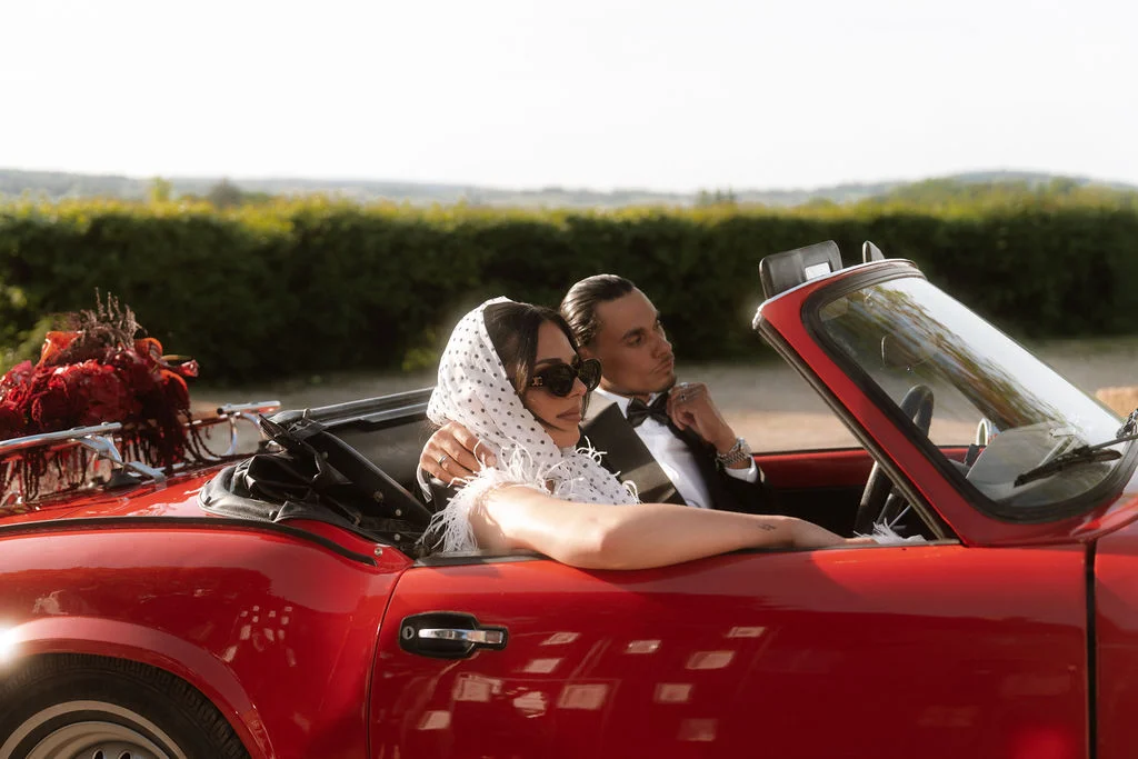 Un couple romantique dans une voiture rouge vintage, célébrant leur mariage avec grâce et élégance.