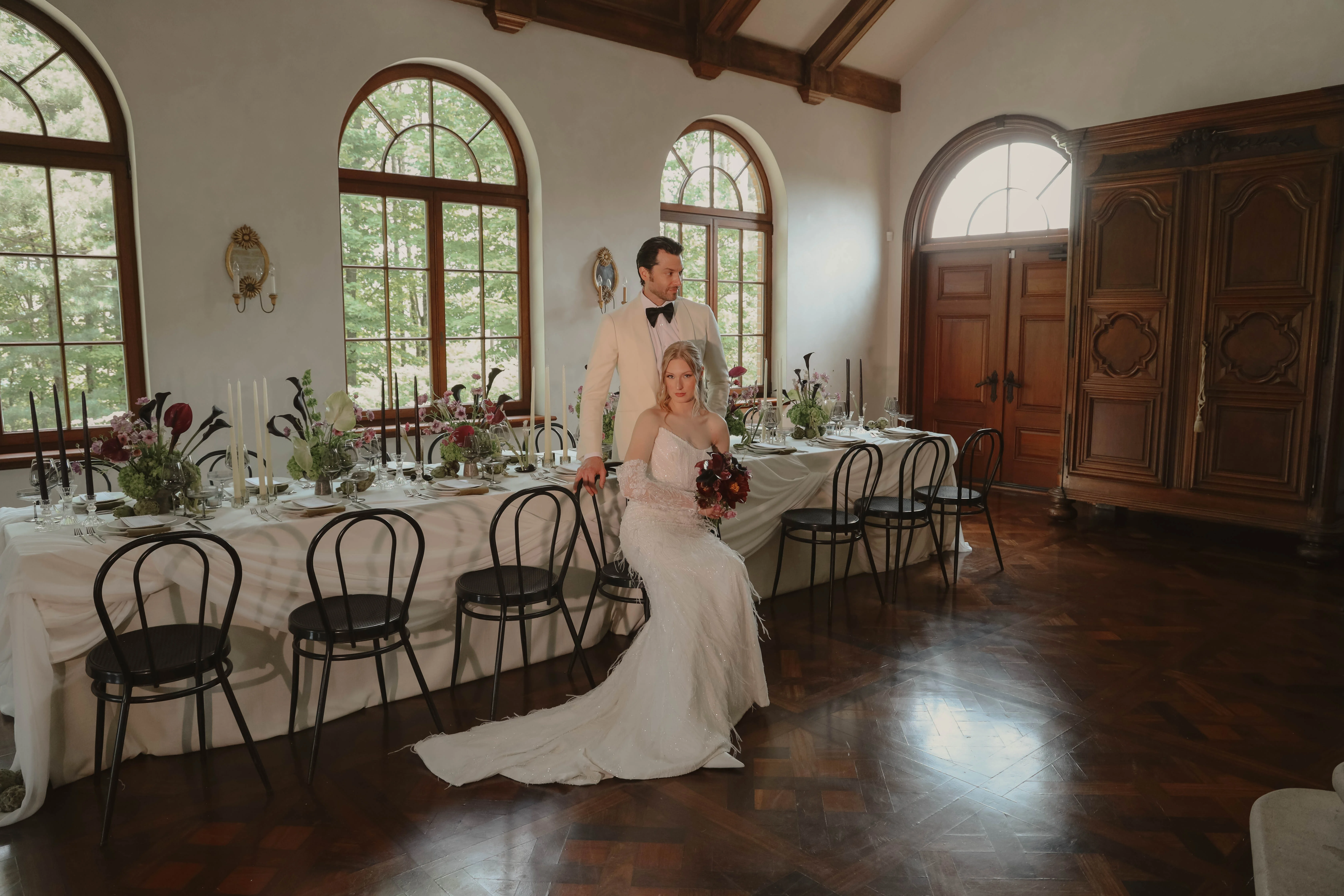 Couple marié élégant posant près d'une table minimaliste dans un salon lumineux aux tons boisés et blancs.