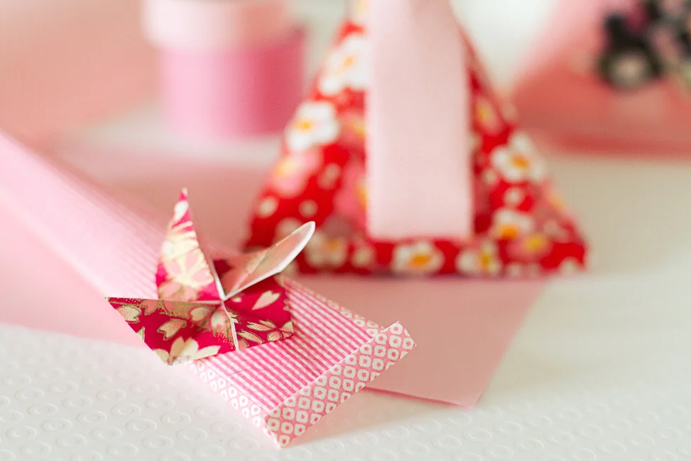 Petits berlingots et origami en papier rose et rouge à motifs floraux pour une décoration de mariage romantique.