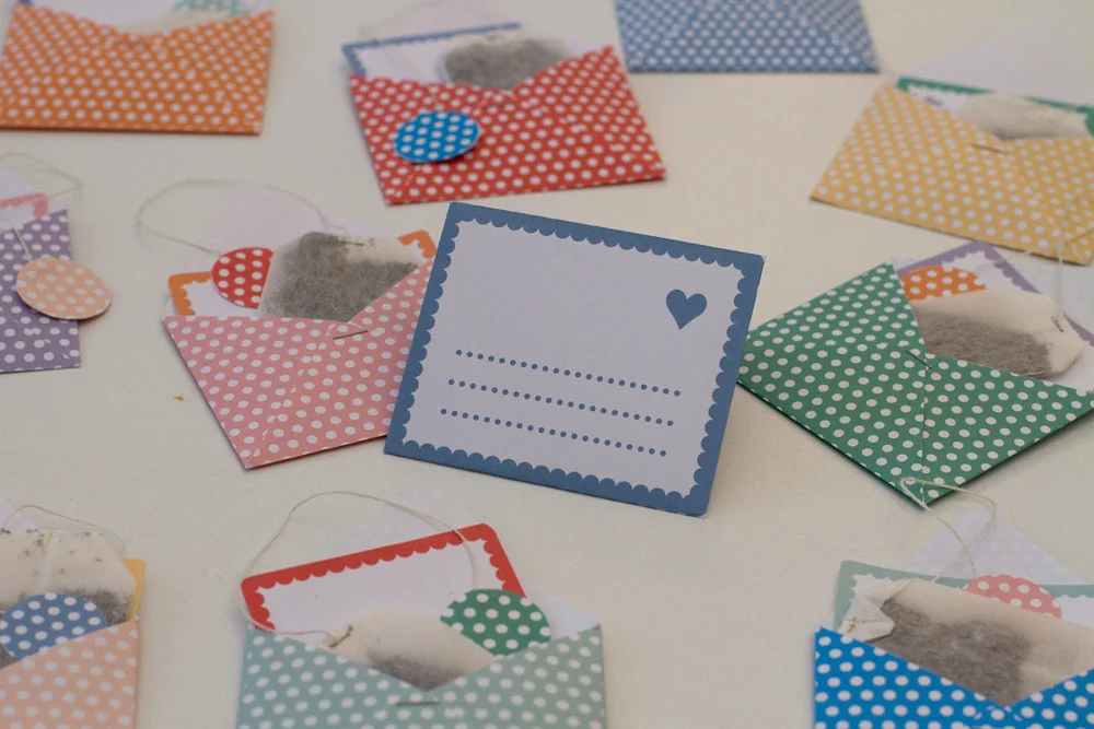 Petites enveloppes colorées à pois contenant des sachets de thé, disposées sur un fond blanc.