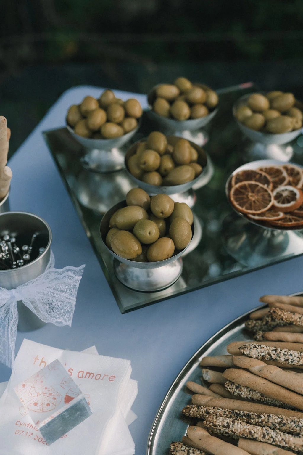 Plusieurs bols d'olives vertes disposés sur un plateau miroir lors d'un cocktail de mariage élégant.