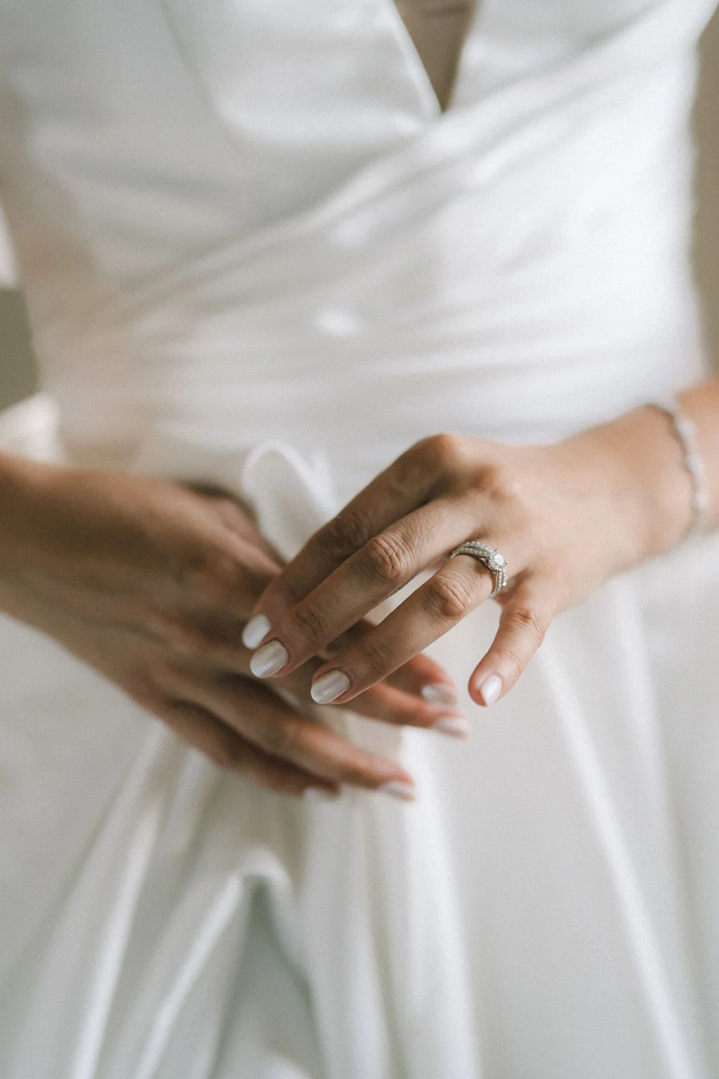 Gros plan sur les mains d'une mariée en robe blanche, mettant en valeur son alliance et son solitaire étincelants.