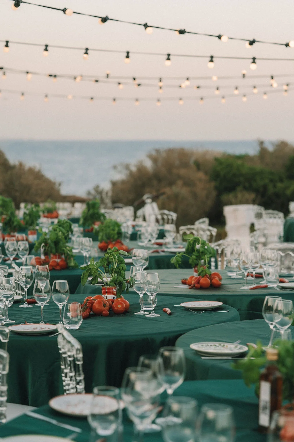 Tables de mariage élégantes nappées de vert avec décorations de tomates et guirlandes lumineuses en extérieur.