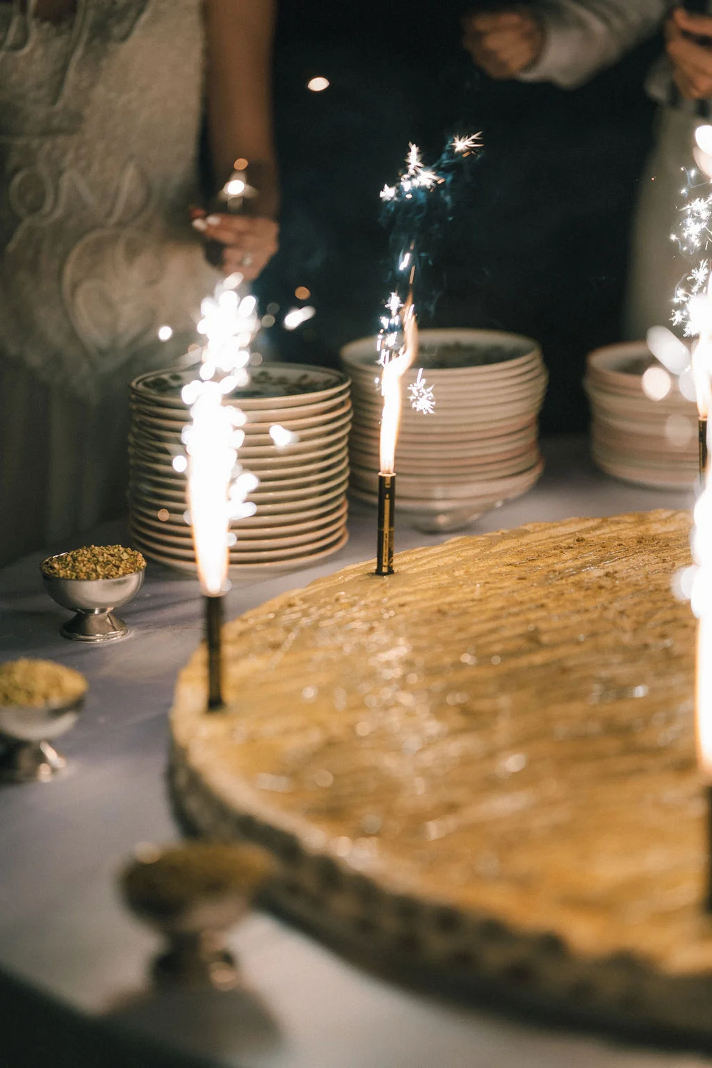 Gros plan d'un gâteau de mariage doré illuminé par des cierges magiques sur une table élégante.