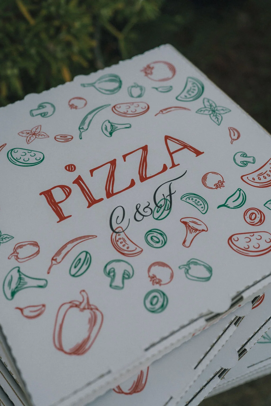 Boîtes de pizza blanches décorées d'illustrations de légumes rouges et verts avec l'inscription Pizza C&F.