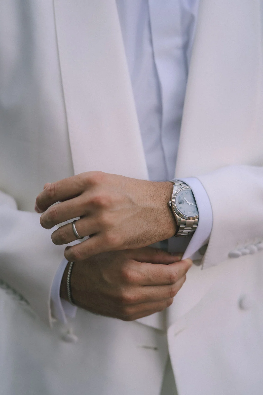 Gros plan sur un marié en costume blanc ajustant sa manche, portant une alliance et une montre argentée.