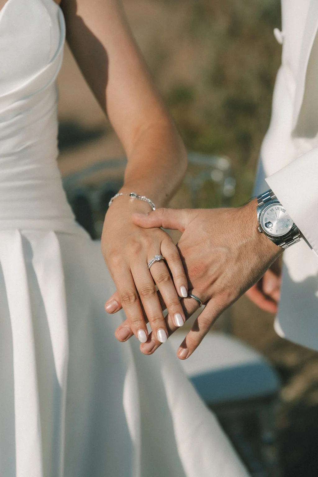 Gros plan romantique sur les mains entrelacées d'un couple marié, mettant en avant leurs alliances et bijoux élégants.